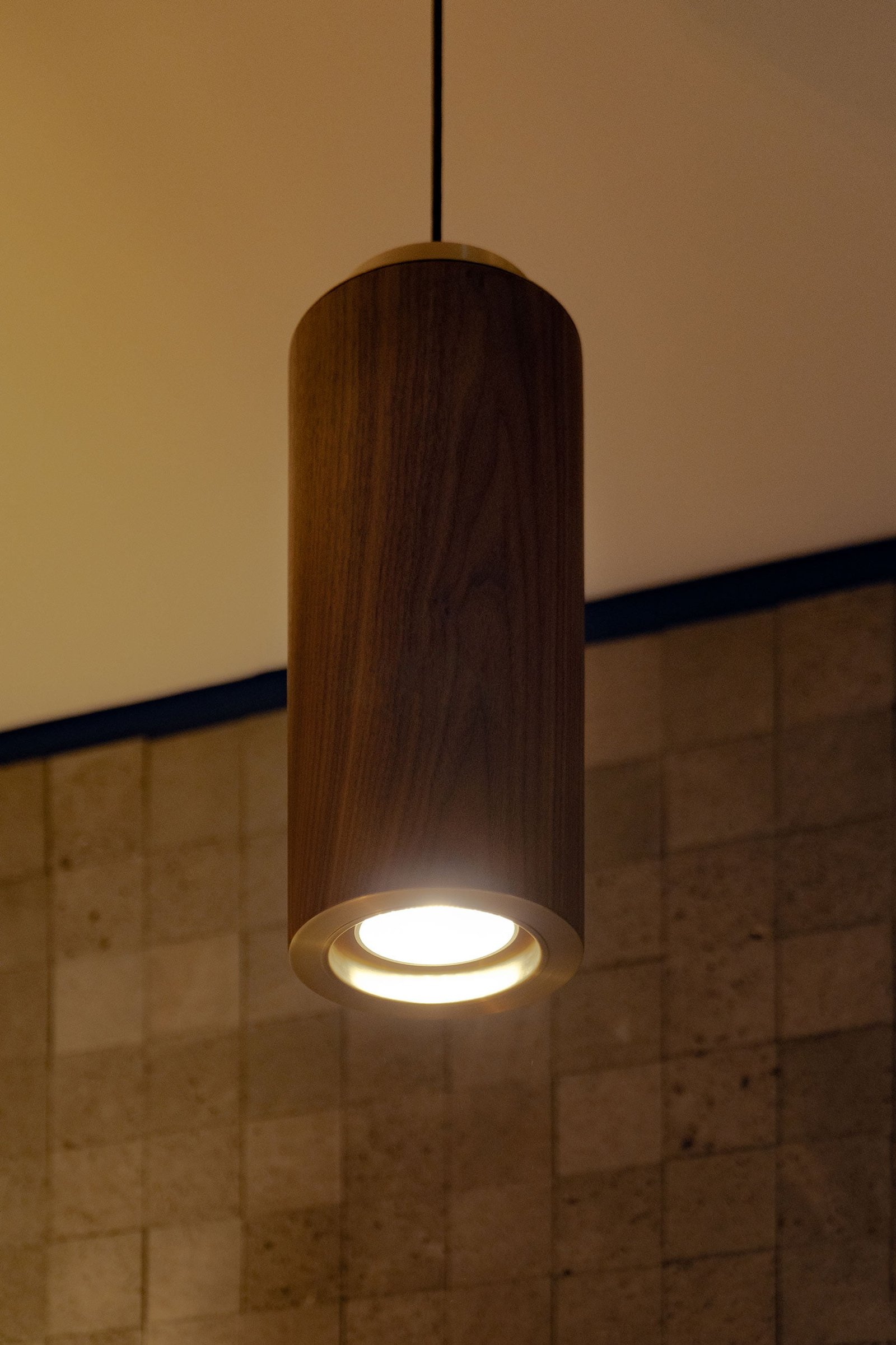 Lámpara colgante de cilindro TEMPLO hecha de madera de nogal y latón diseñada por Bandido Studio en Baño de Mármol en Design House 2023, Design Week México.