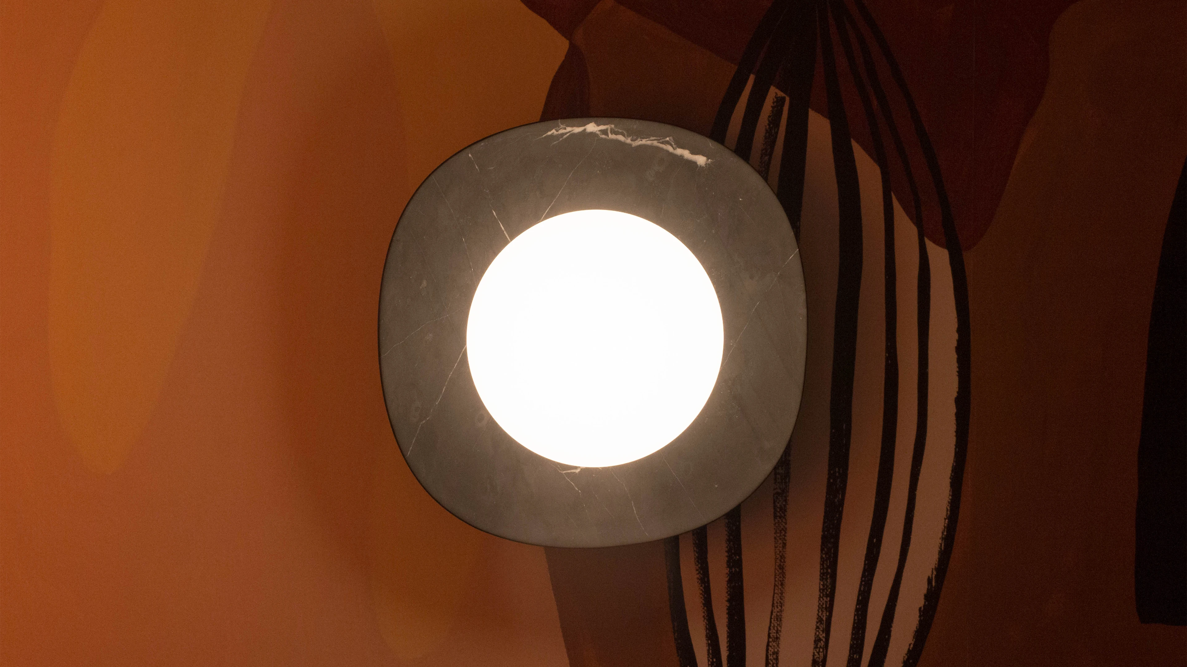 Lámpara de muro NAGA disco de mármol negro y difusor de vidrio con luz cálida, diseñada por Bandido Studio, en habitación naranja, en Design House 2022, Design Week México.