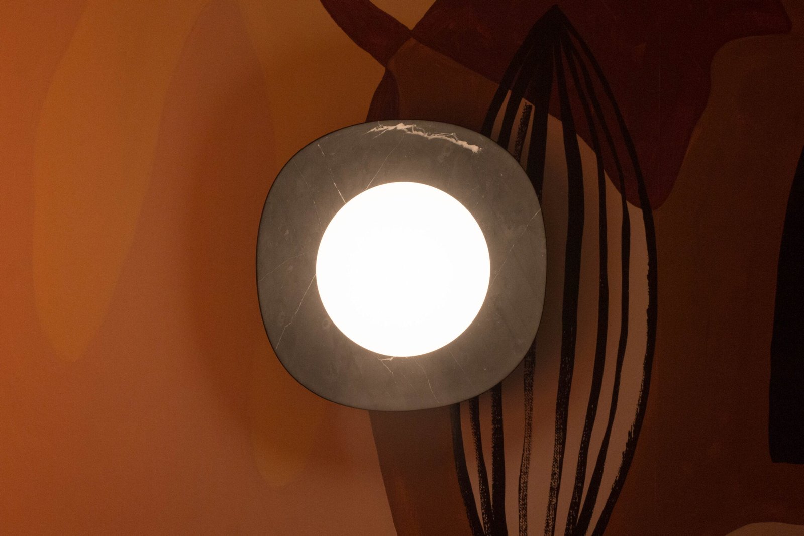 Lámpara de muro NAGA disco de mármol negro y difusor de vidrio con luz cálida, diseñada por Bandido Studio, en habitación naranja, en Design House 2022, Design Week México.